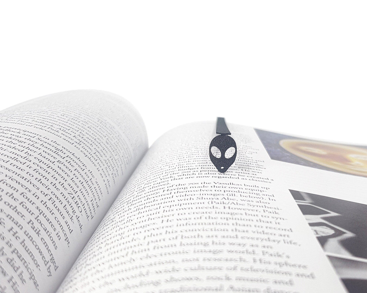 Alien Head metal bookmark resting on the pages of an open book
