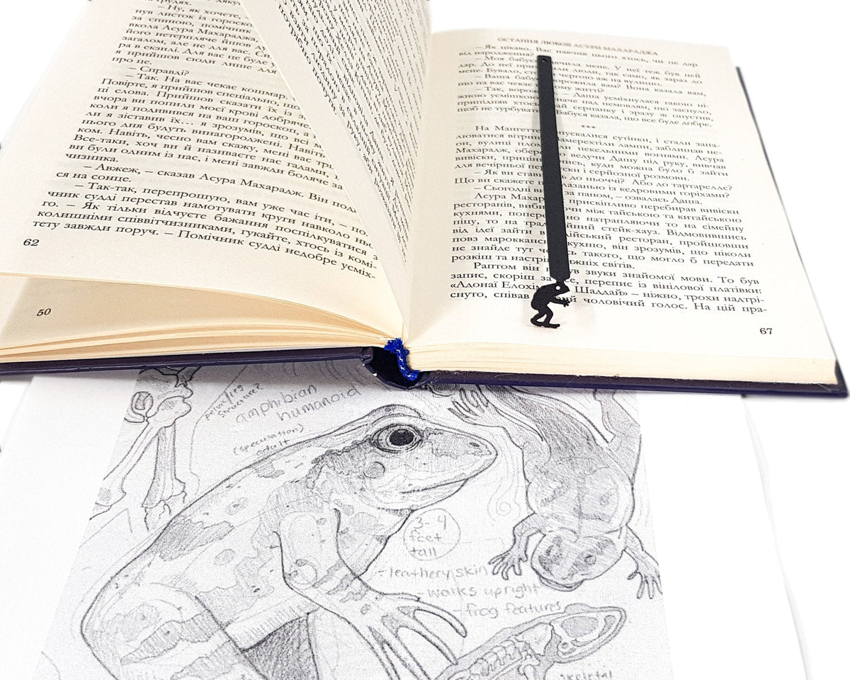 Frogman metal bookmark marking a page in an illustrated book, view 4