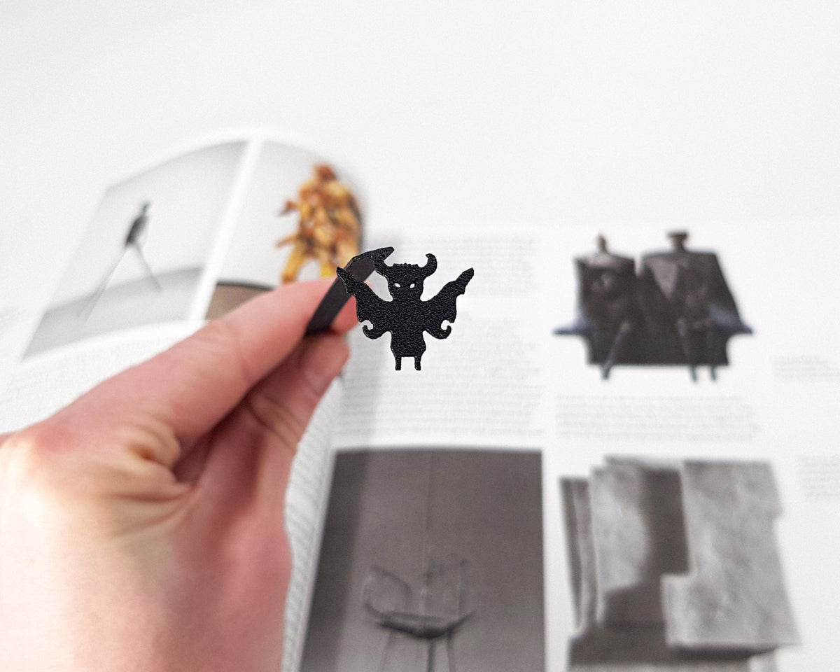 Monster Chupacabra metal bookmark held in a hand above an open book