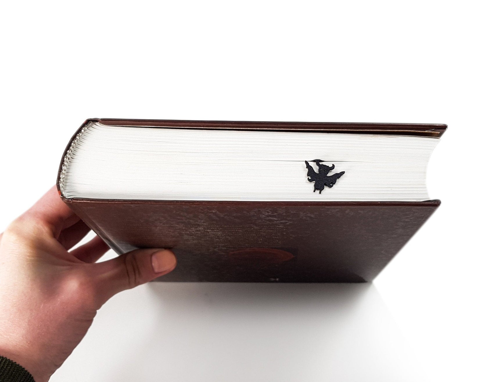 Monster Chupacabra metal bookmark held up beside an open book