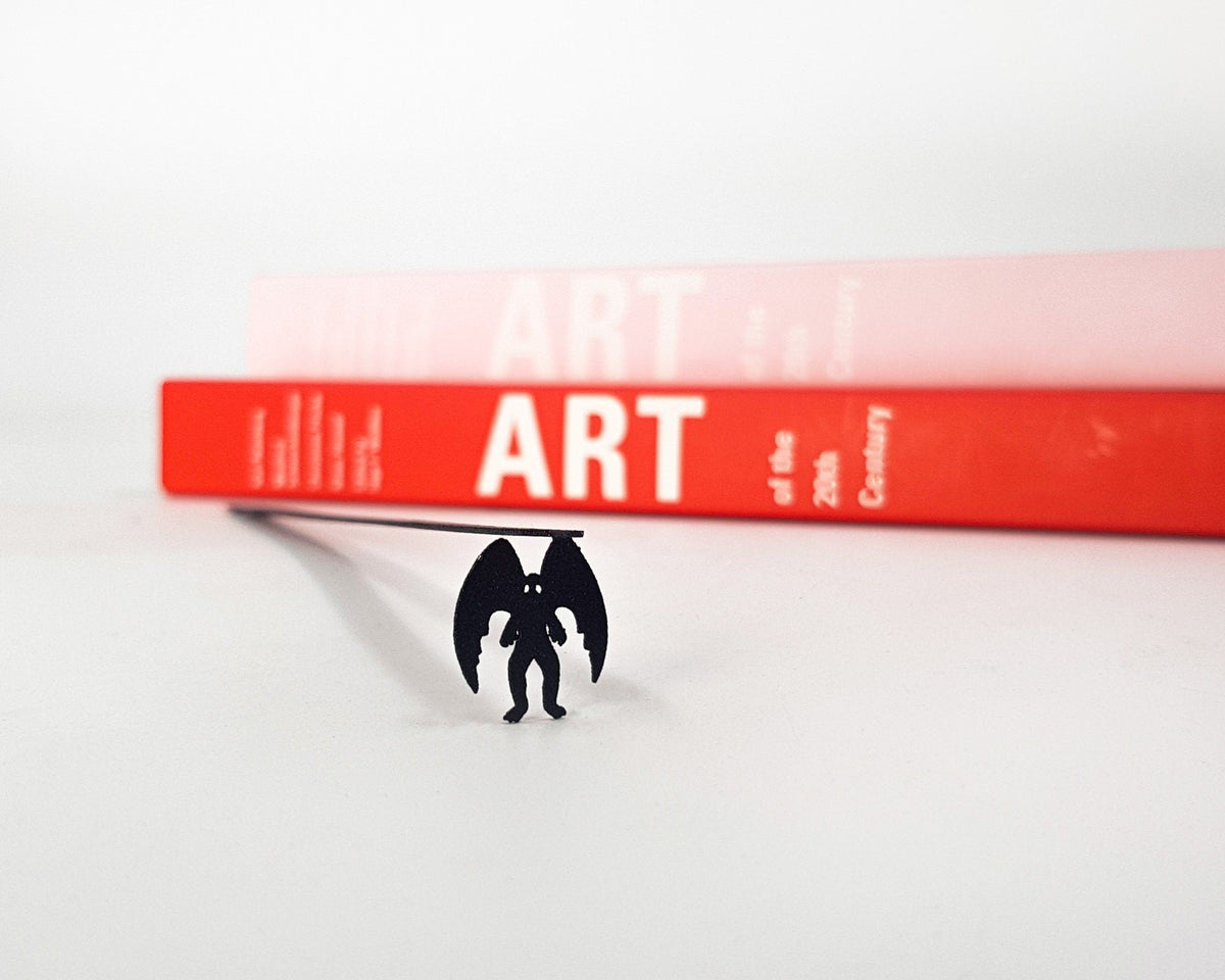 Mothman metal bookmark in a closed book, only its top showing above the pages