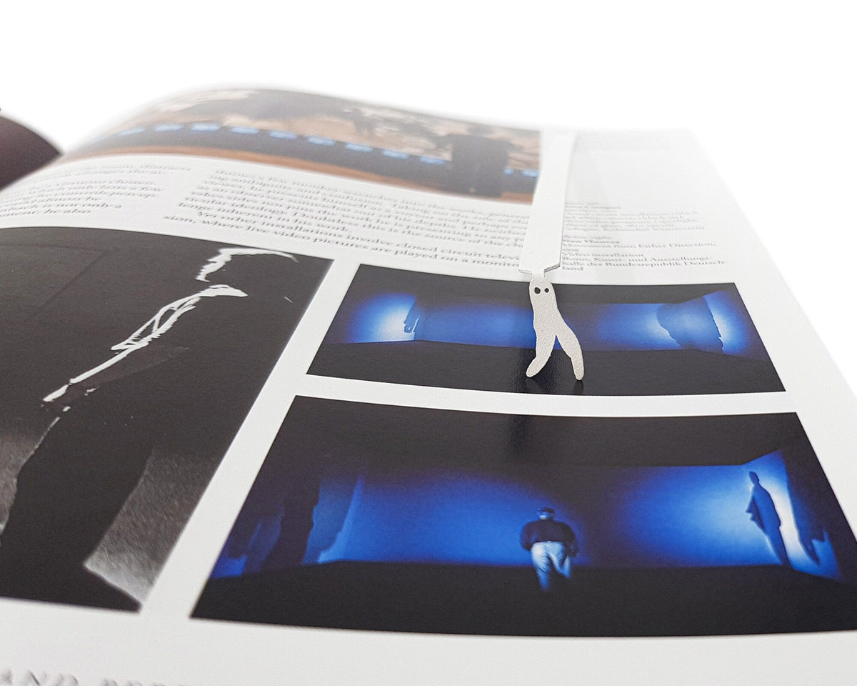 Nightcrawler metal bookmark in white marking a page in an illustrated book, view 4