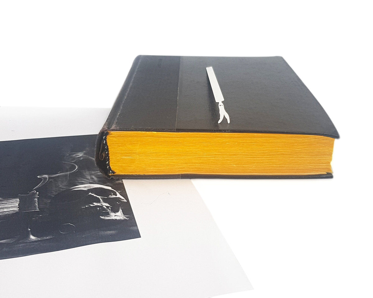 Nightcrawler metal bookmark in white in a closed book, only its top showing above the pages, view 5