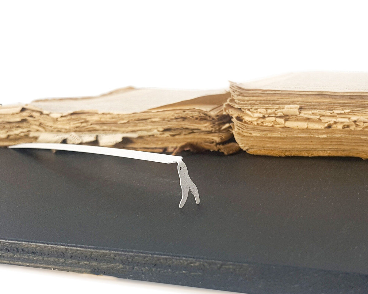Nightcrawler metal bookmark in white marking a place in a closed book