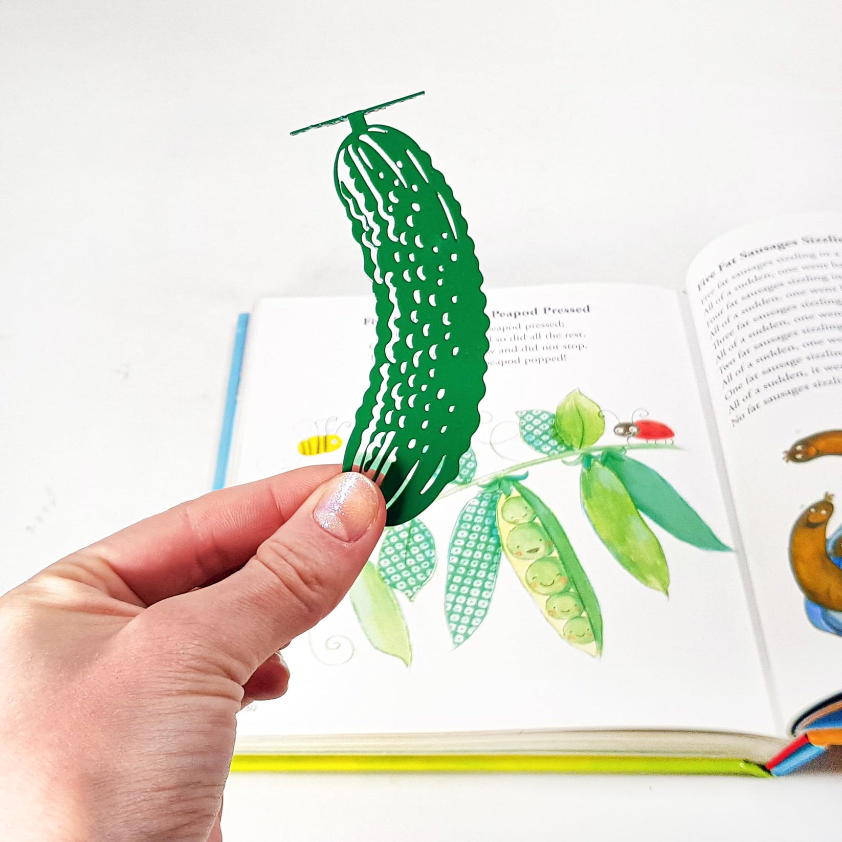 Cucumber metal bookmark in green held in a hand above an open book