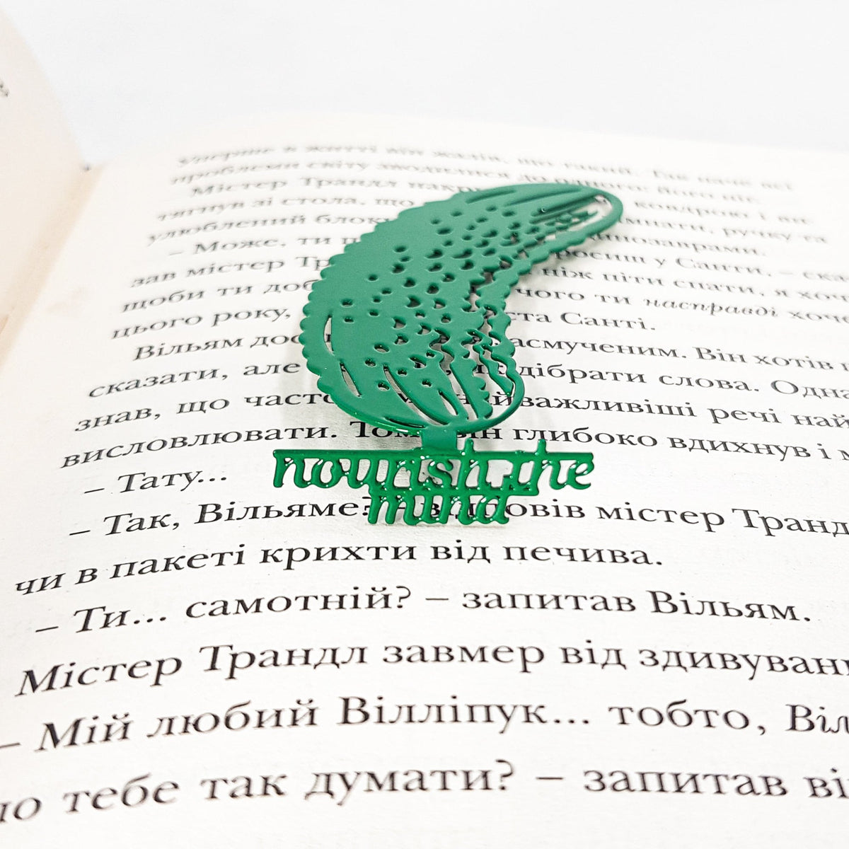 Cucumber metal bookmark in green lying across the pages of an open book
