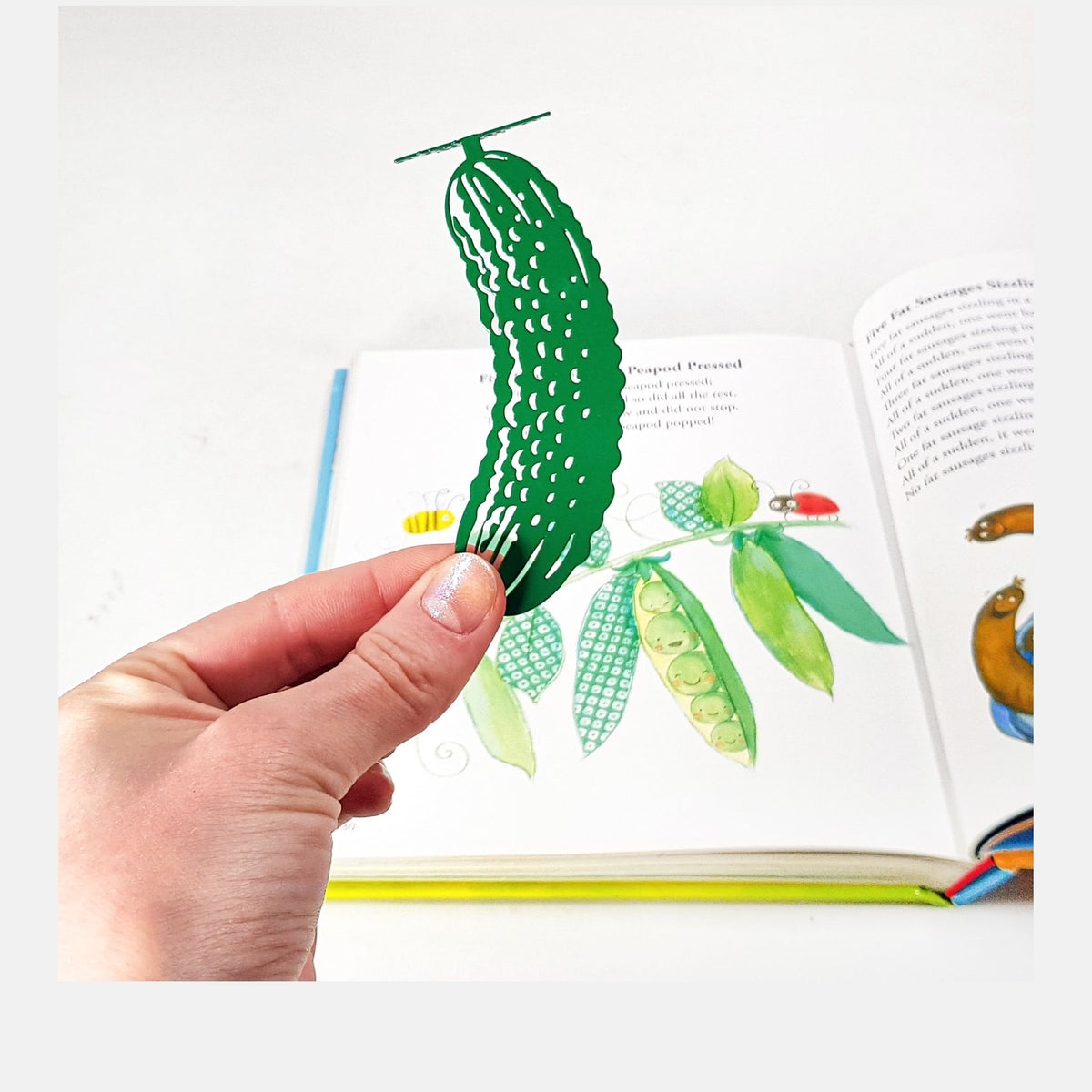Cucumber metal bookmark in green held in a hand above an open book