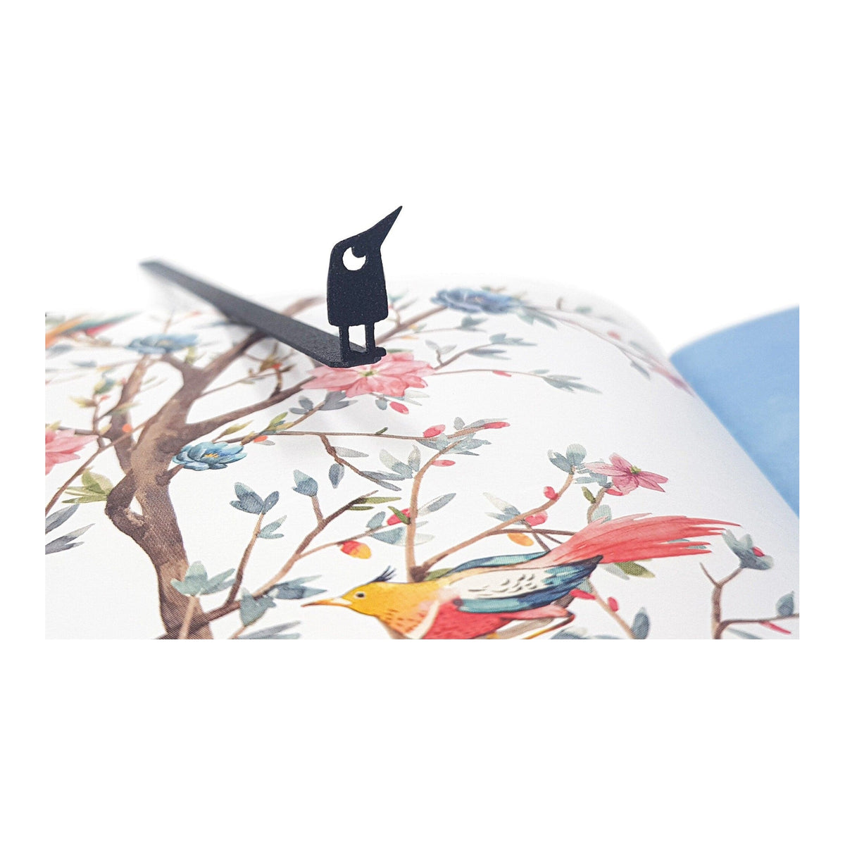 Curious Bird metal bookmark marking a page in an illustrated book