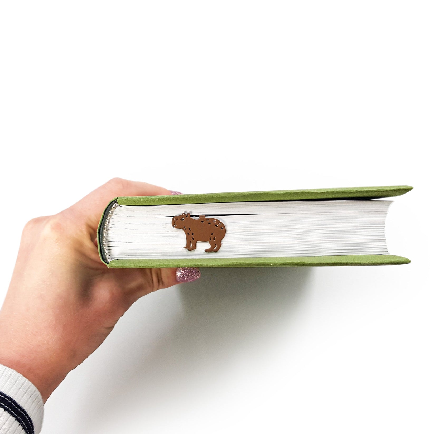 Capybara metal bookmark held in a hand above an open book