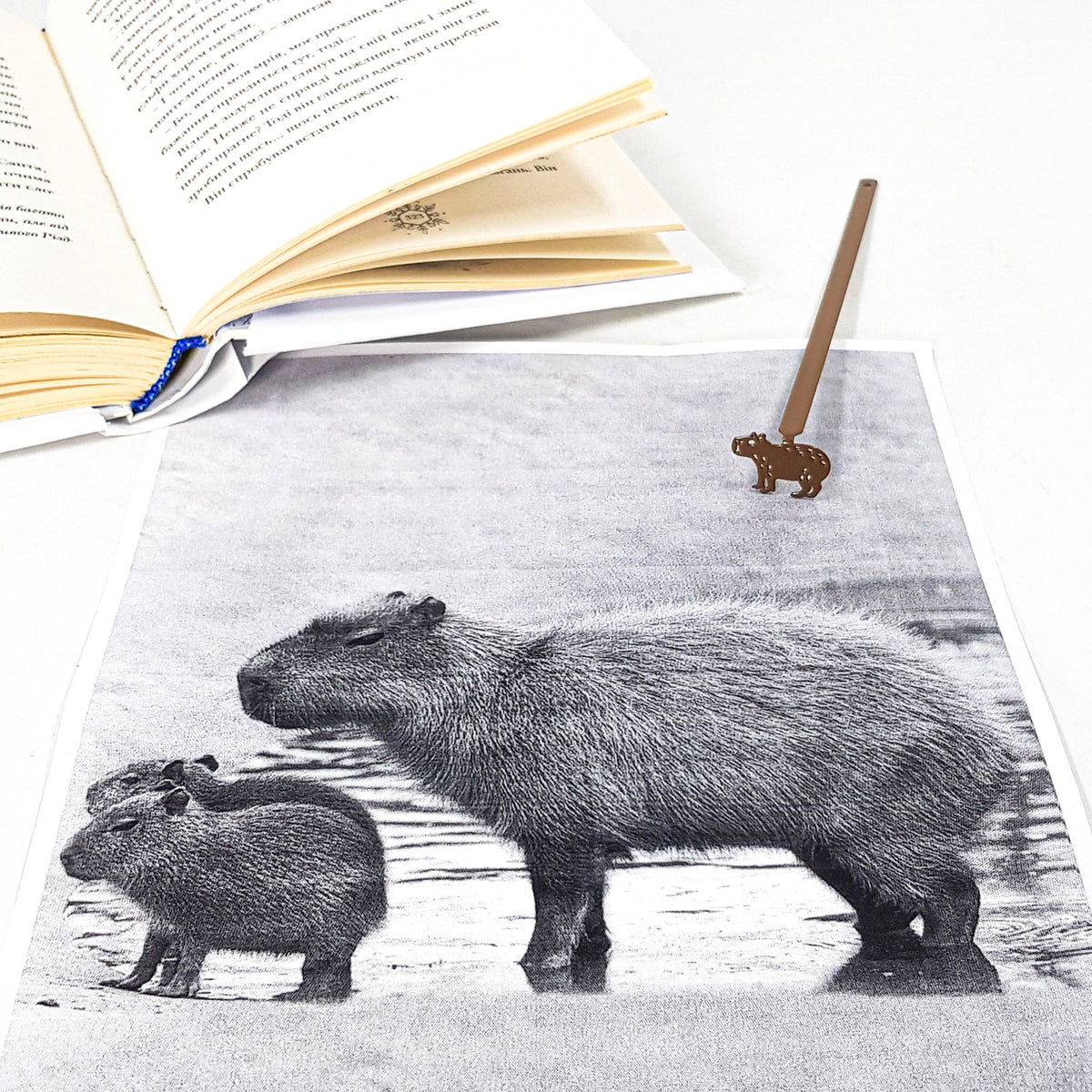 Capybara metal bookmark marking a page in an illustrated book