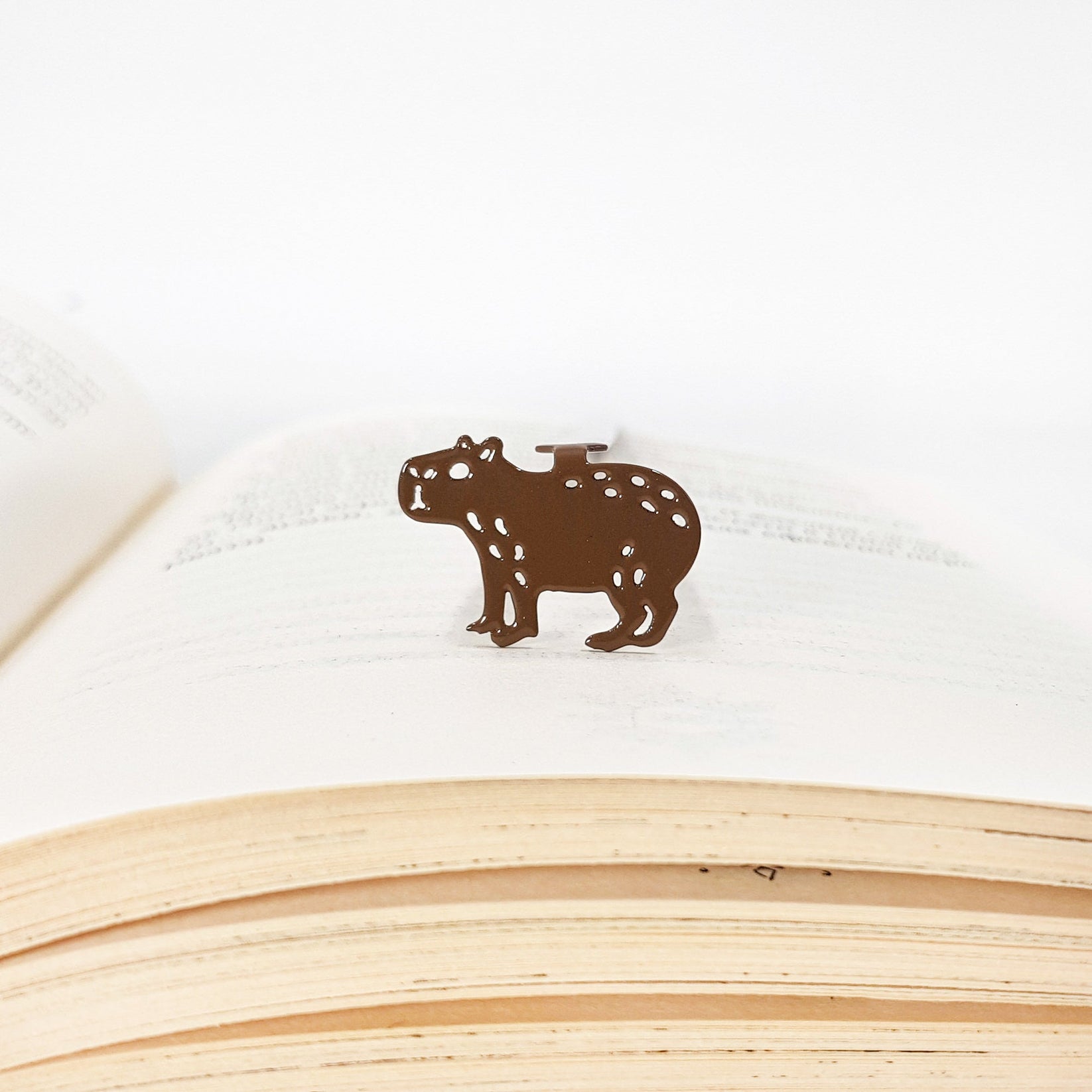 Capybara metal bookmark in a closed book, only its top showing above the pages