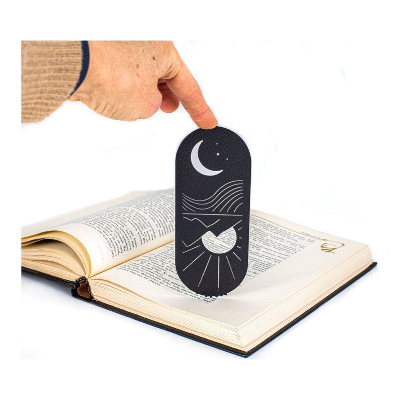 Day and Night, Sun and Moon metal bookmark held in a hand above an open book