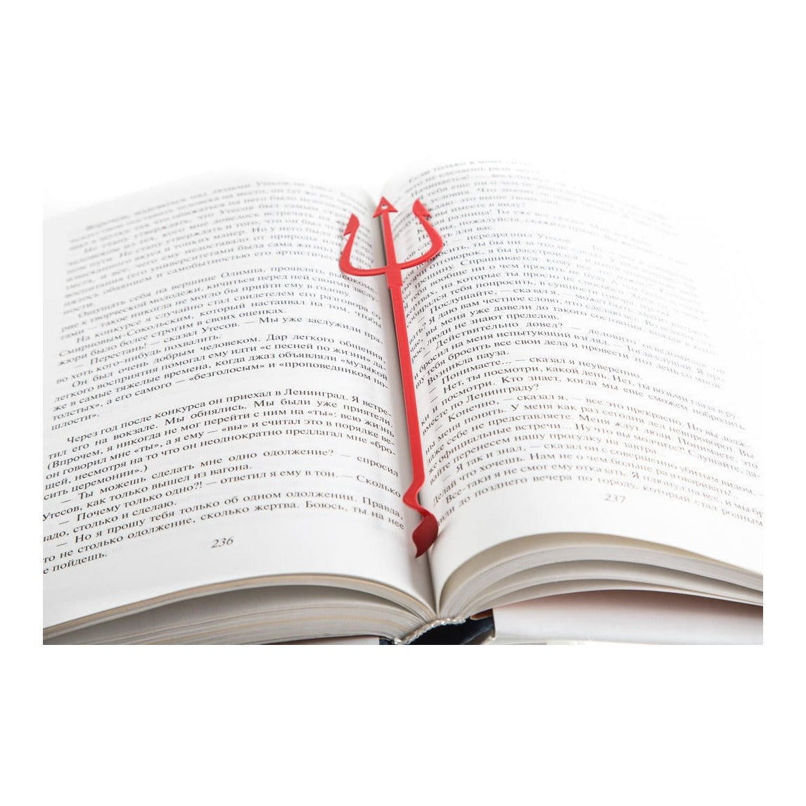 Devil's Trident metal bookmark in red resting on the pages of an open book