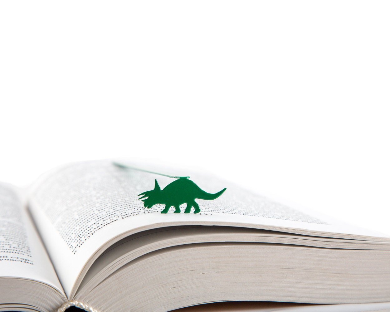 Dinosaur Trice raptor metal bookmark in green resting on the pages of an open book