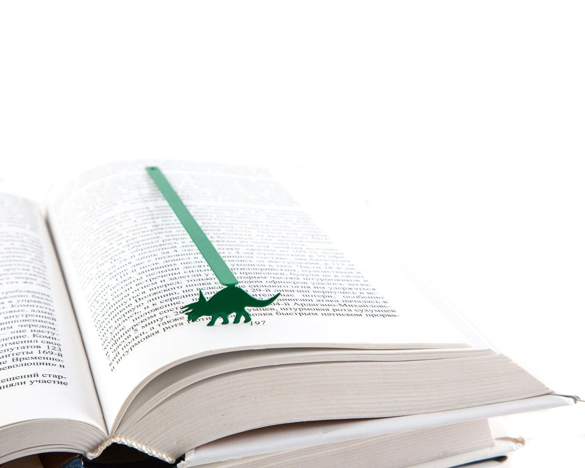 Dinosaur Trice raptor metal bookmark in green marking a page in an open book
