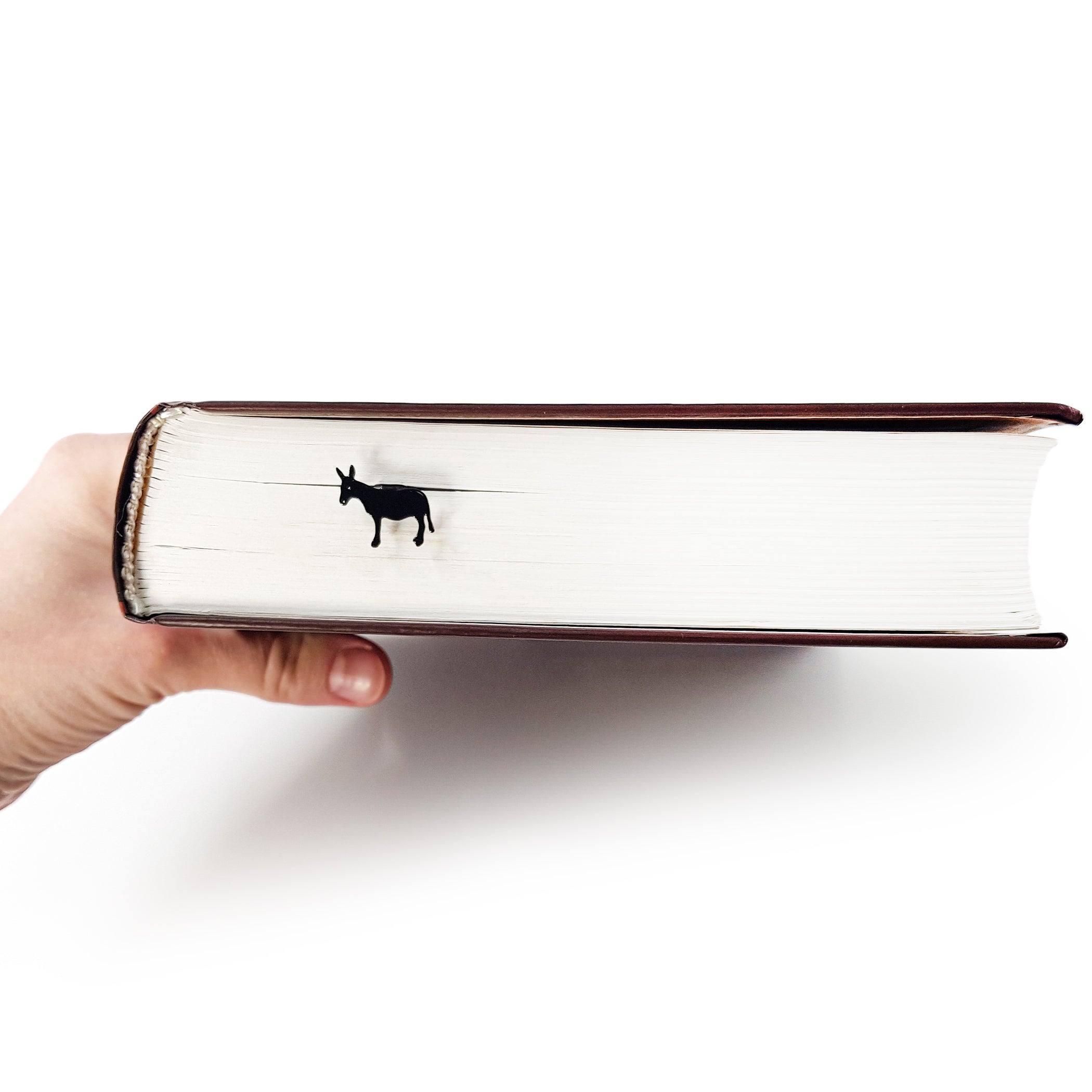 Hand holding thick hardcover book sideways with black donkey bookmark peeking from top edge