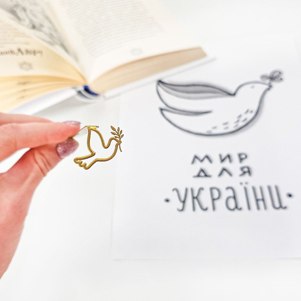 Dove of Peace metal bookmark in gold held up beside an open book