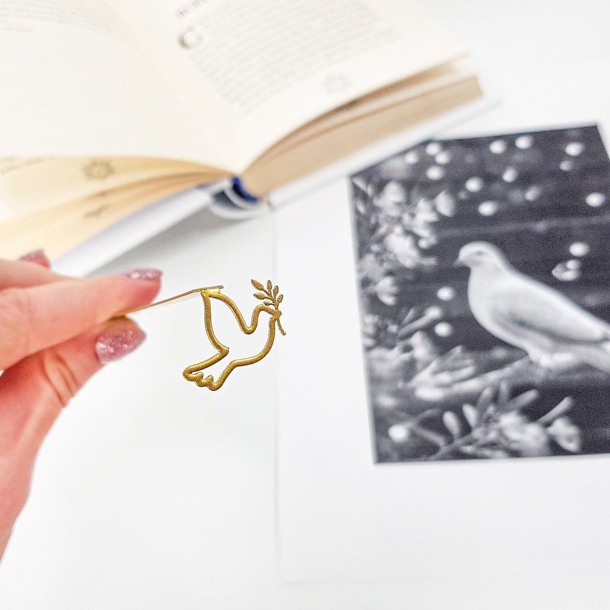Dove of Peace metal bookmark in gold held in a hand above an open book