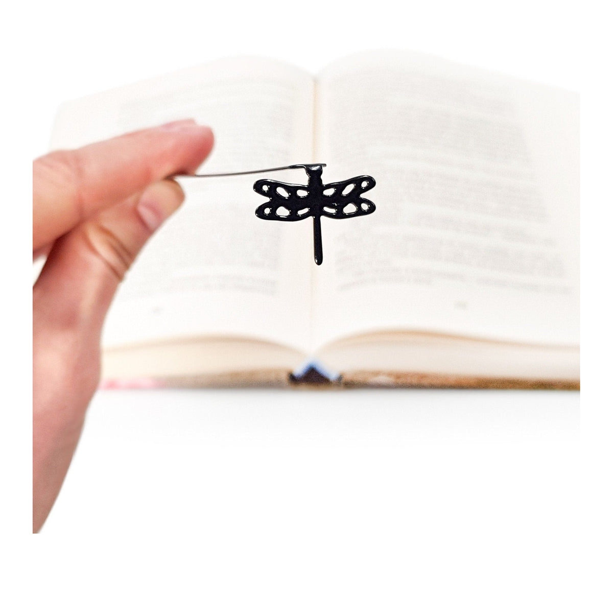 Dragonfly metal bookmark held in a hand above an open book