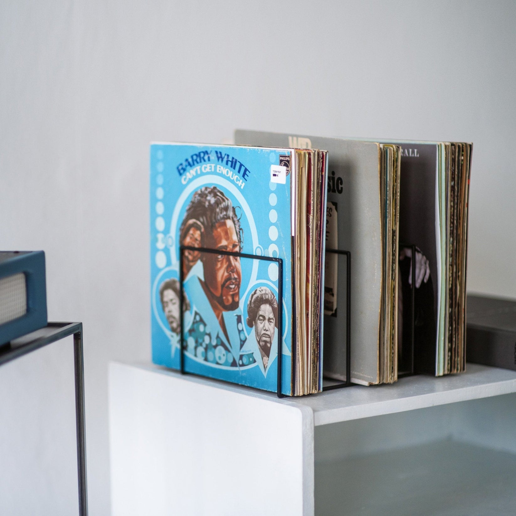Close-up of a black metal vinyl record divider holding a collection of vintage records on a white shelf, with Barry White’s “Can’t Get Enough” album at the front.