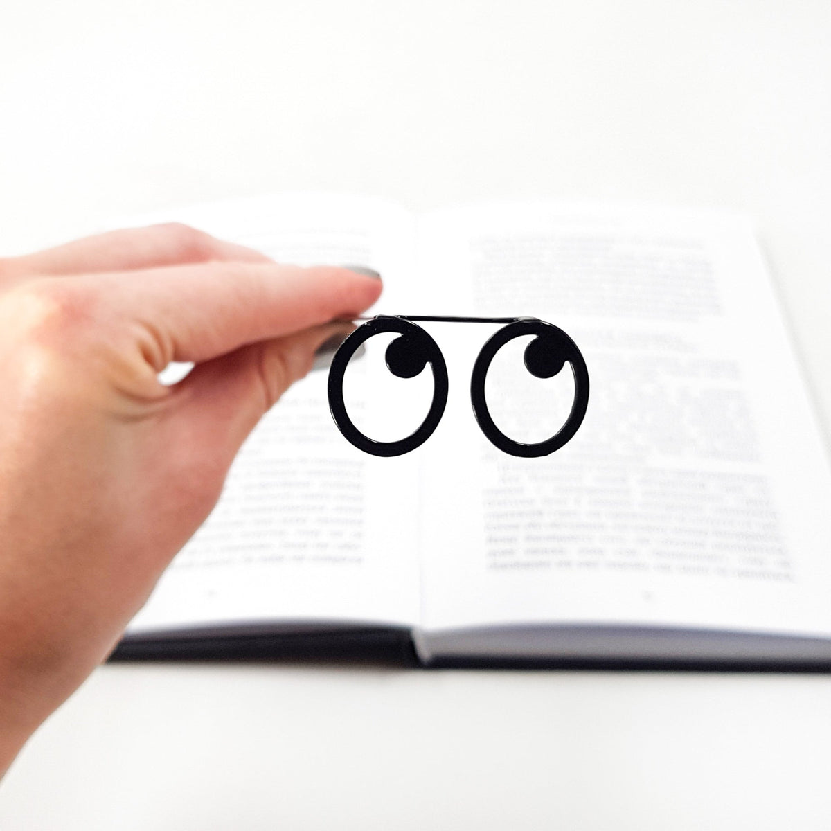 Eyes Glasses metal bookmark held in a hand above an open book