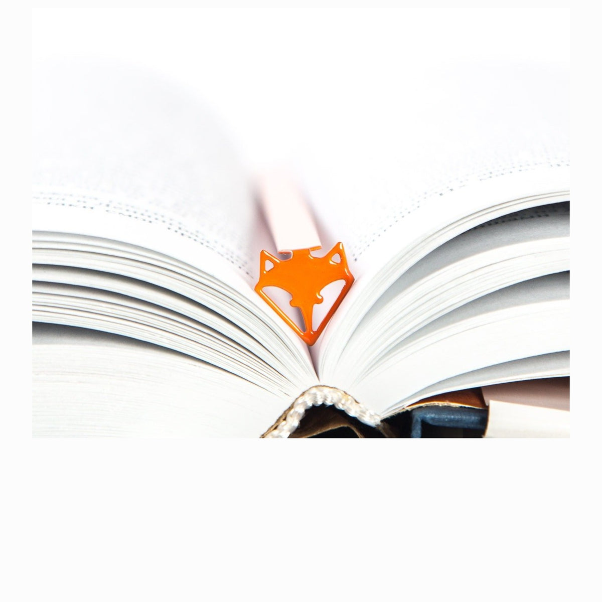 Fox Head metal bookmark in red resting on the pages of an open book