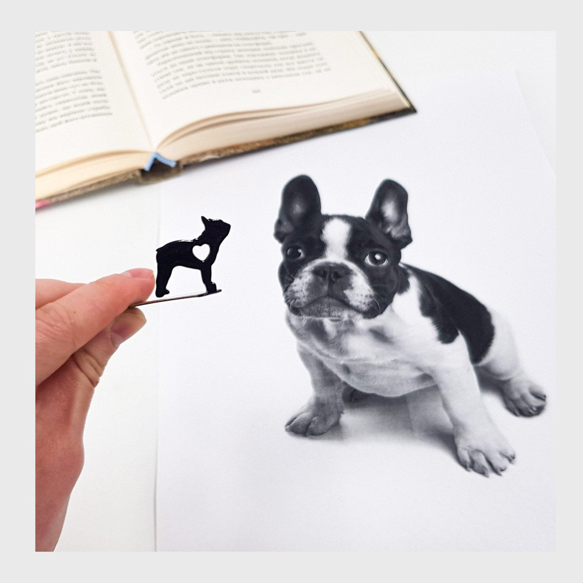 French Bulldog Love metal bookmark held in a hand above an open book