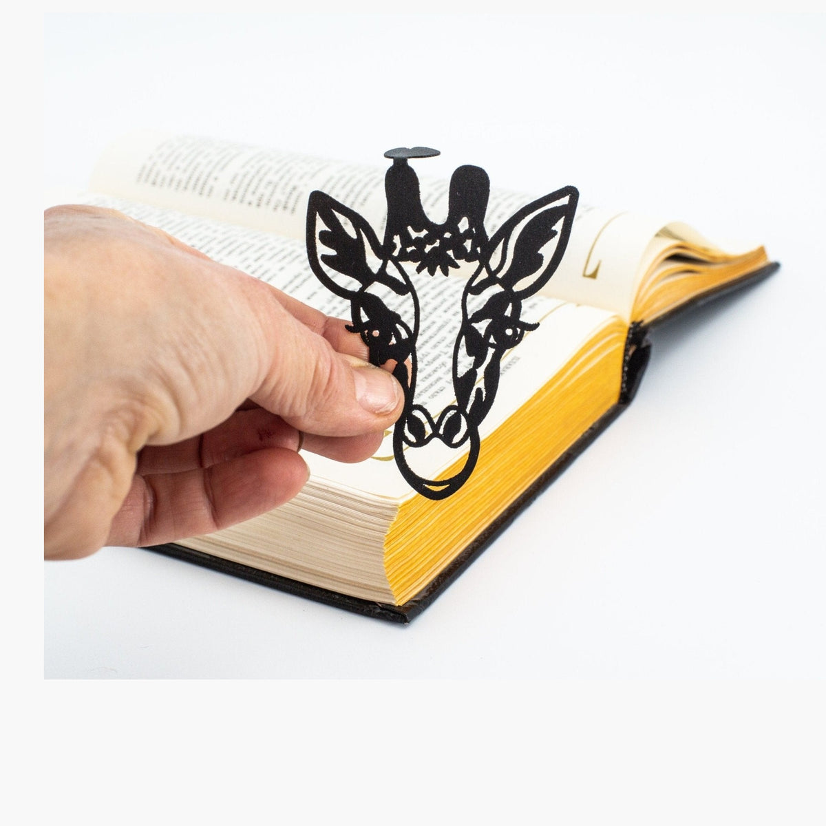 Giraffe Head metal bookmark held in a hand above an open book