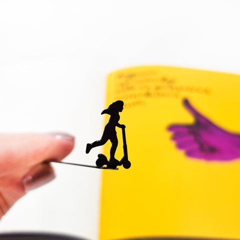 Girl on a Scooter metal bookmark held in a hand above an open book