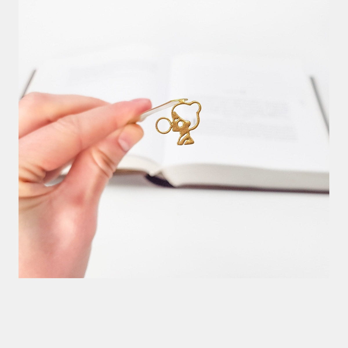 Girl with a Bubble Gum metal bookmark in gold held in a hand above an open book