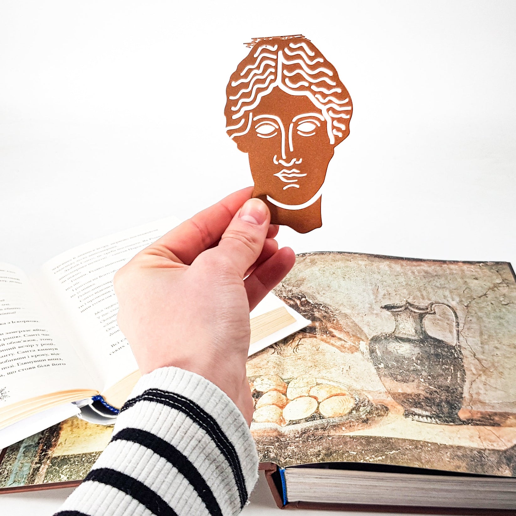 Goddess of Words metal bookmark in red held in a hand to show its size
