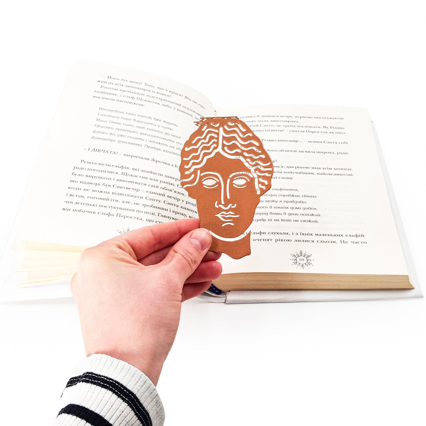 Goddess of Words metal bookmark in red held in a hand above an open book