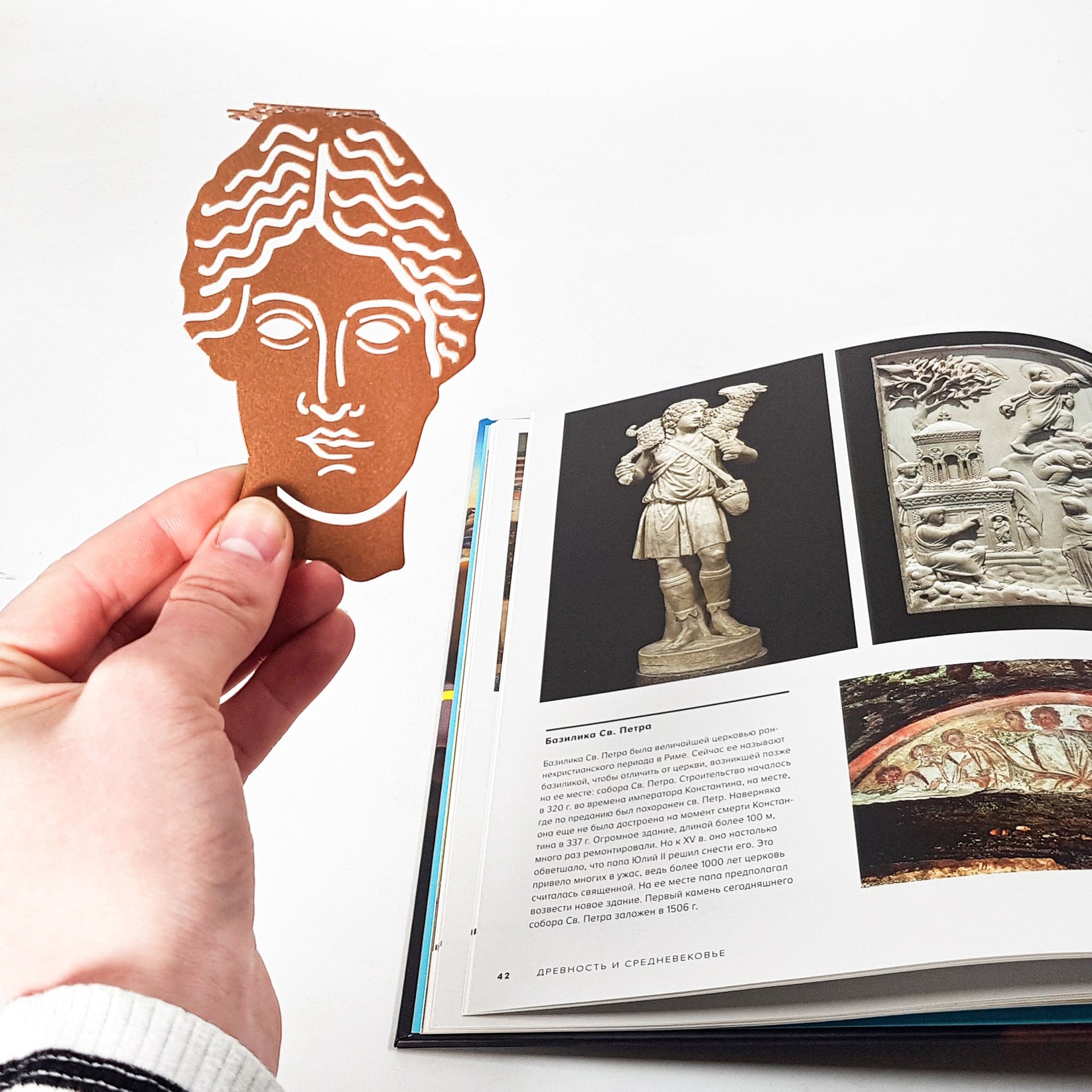 Goddess of Words metal bookmark in red held up beside an open book