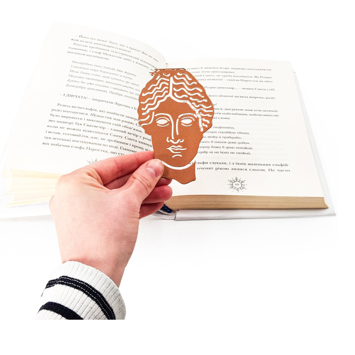 Goddess of Words metal bookmark in red held in a hand above an open book