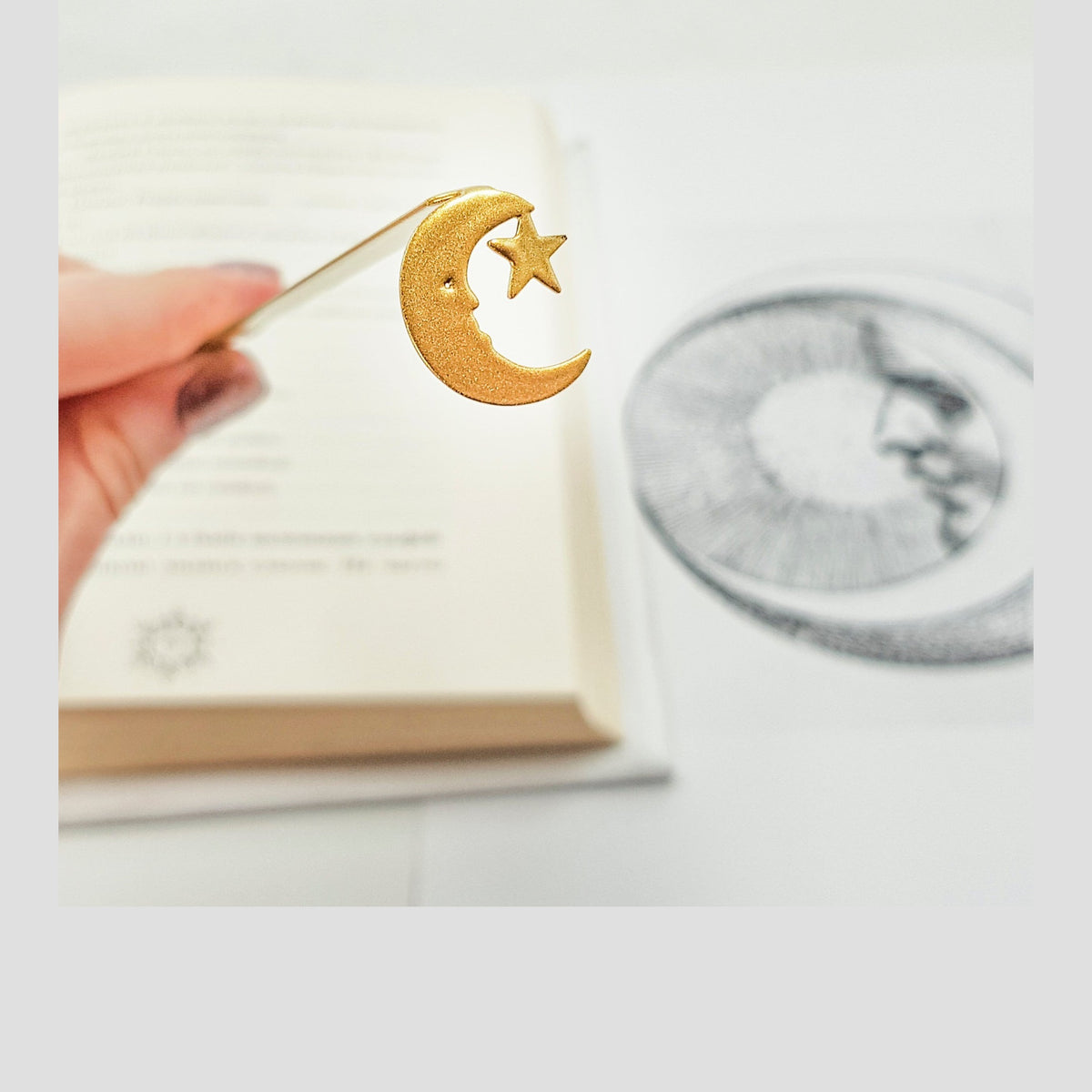 Gold Crescent Moon metal bookmark in gold held in a hand above an open book