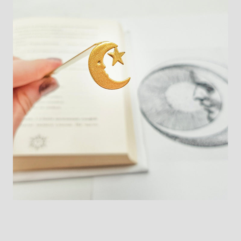 Gold Crescent Moon metal bookmark in gold held in a hand above an open book