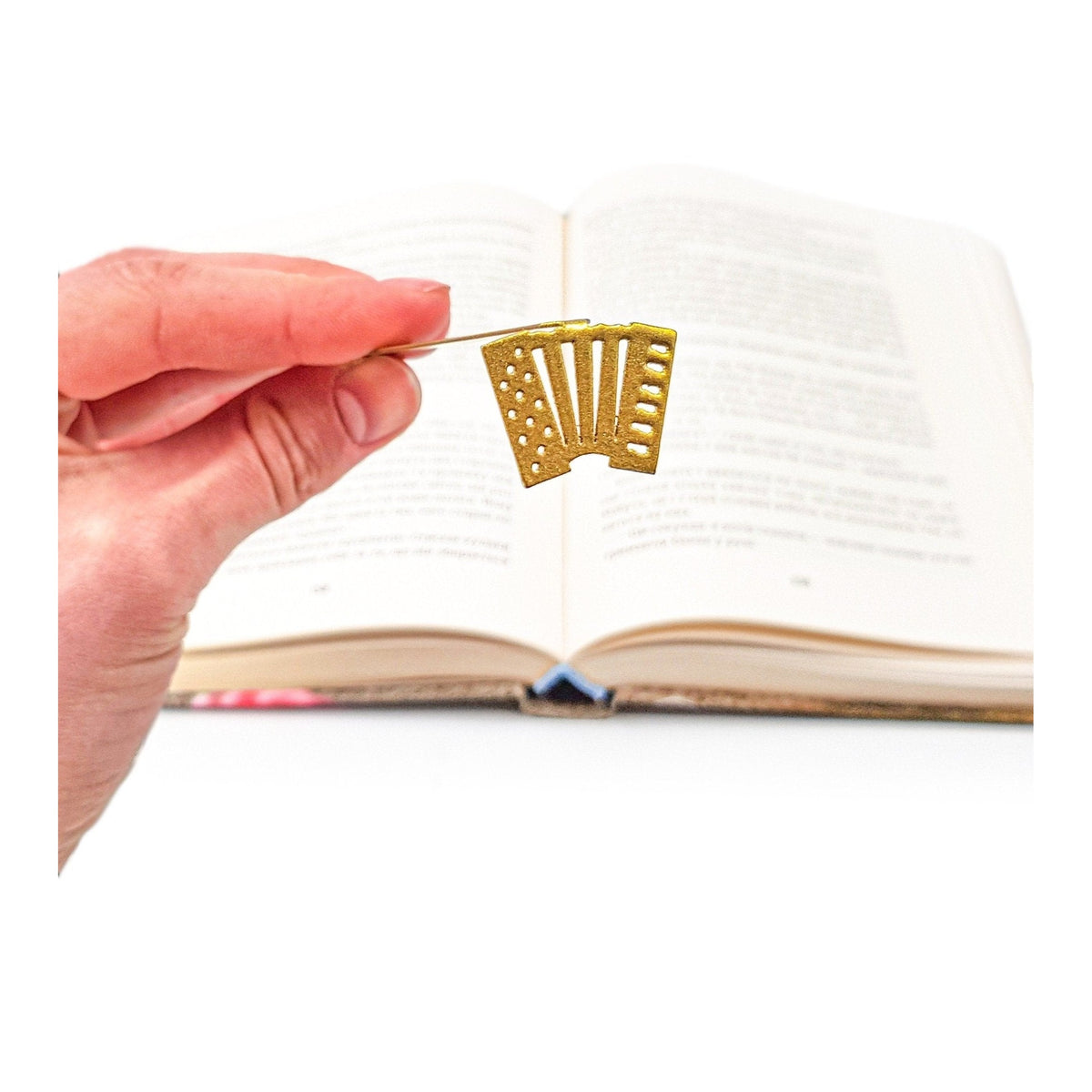 Golden Accordion metal bookmark in gold held in a hand above an open book