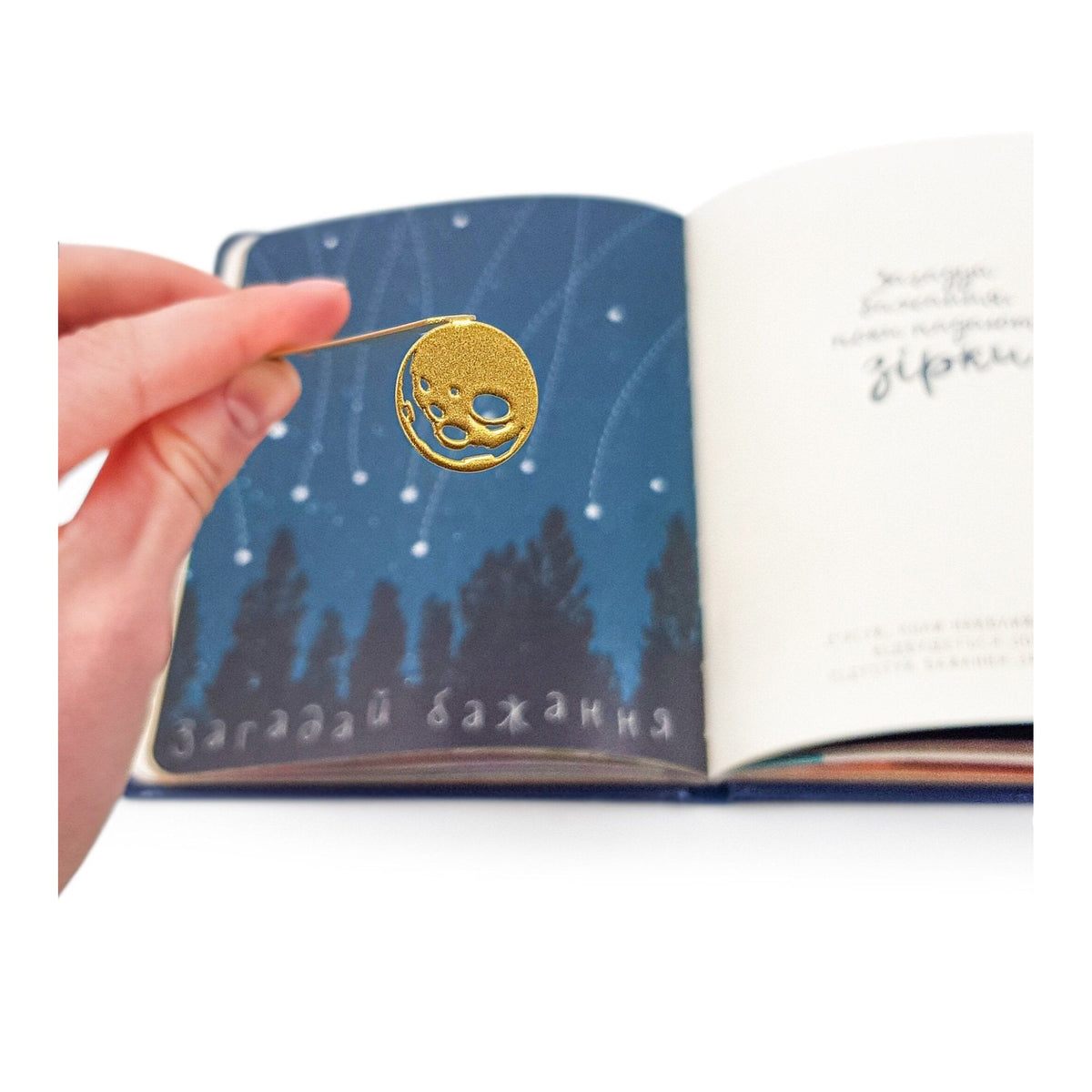 Golden Moon metal bookmark in gold held in a hand above an open book