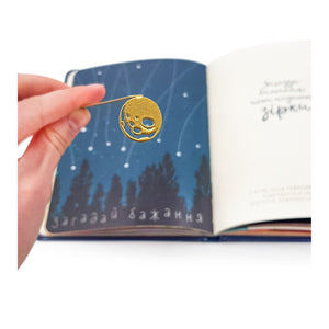 Golden Moon metal bookmark in gold held in a hand above an open book