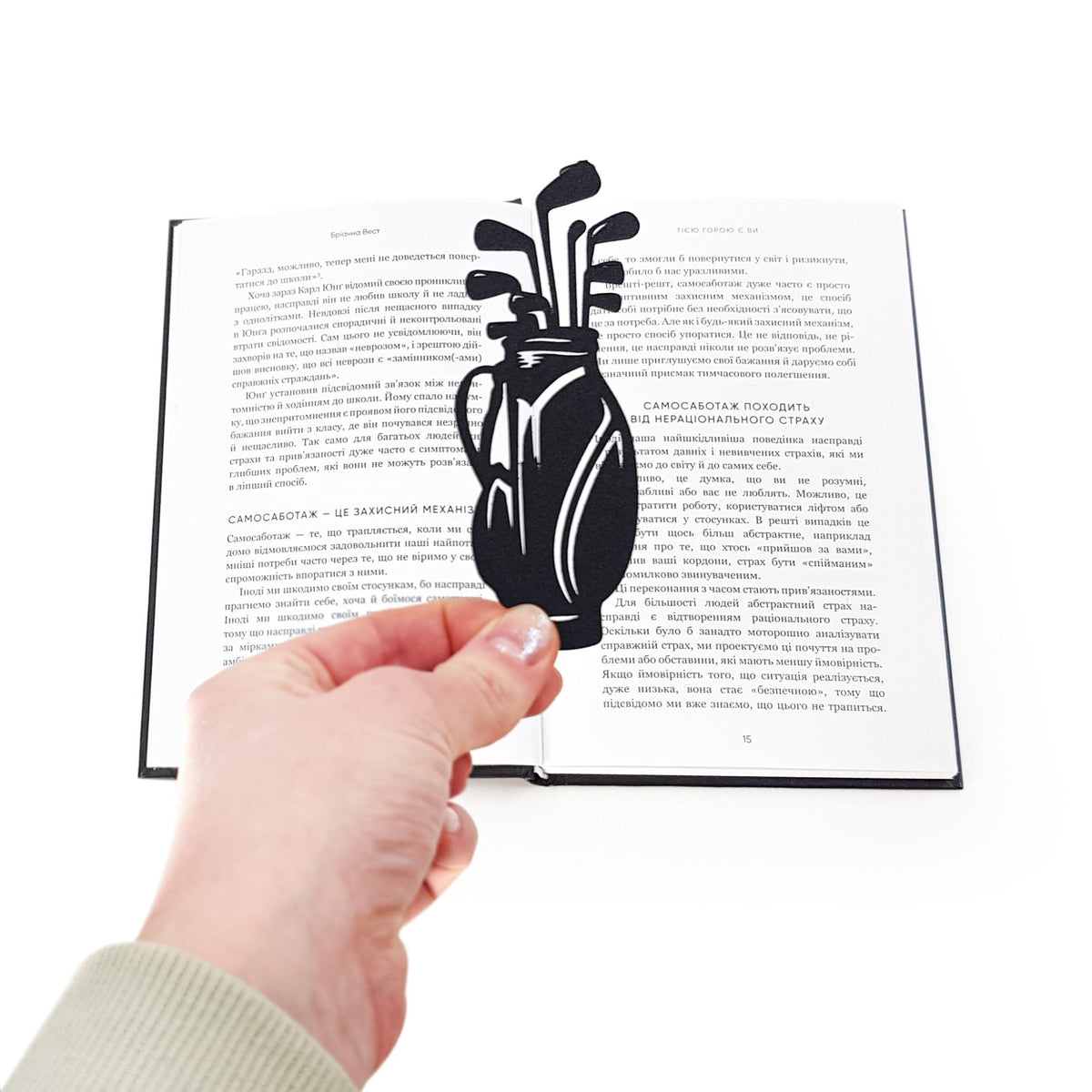 Golf Bag metal bookmark held in a hand above an open book