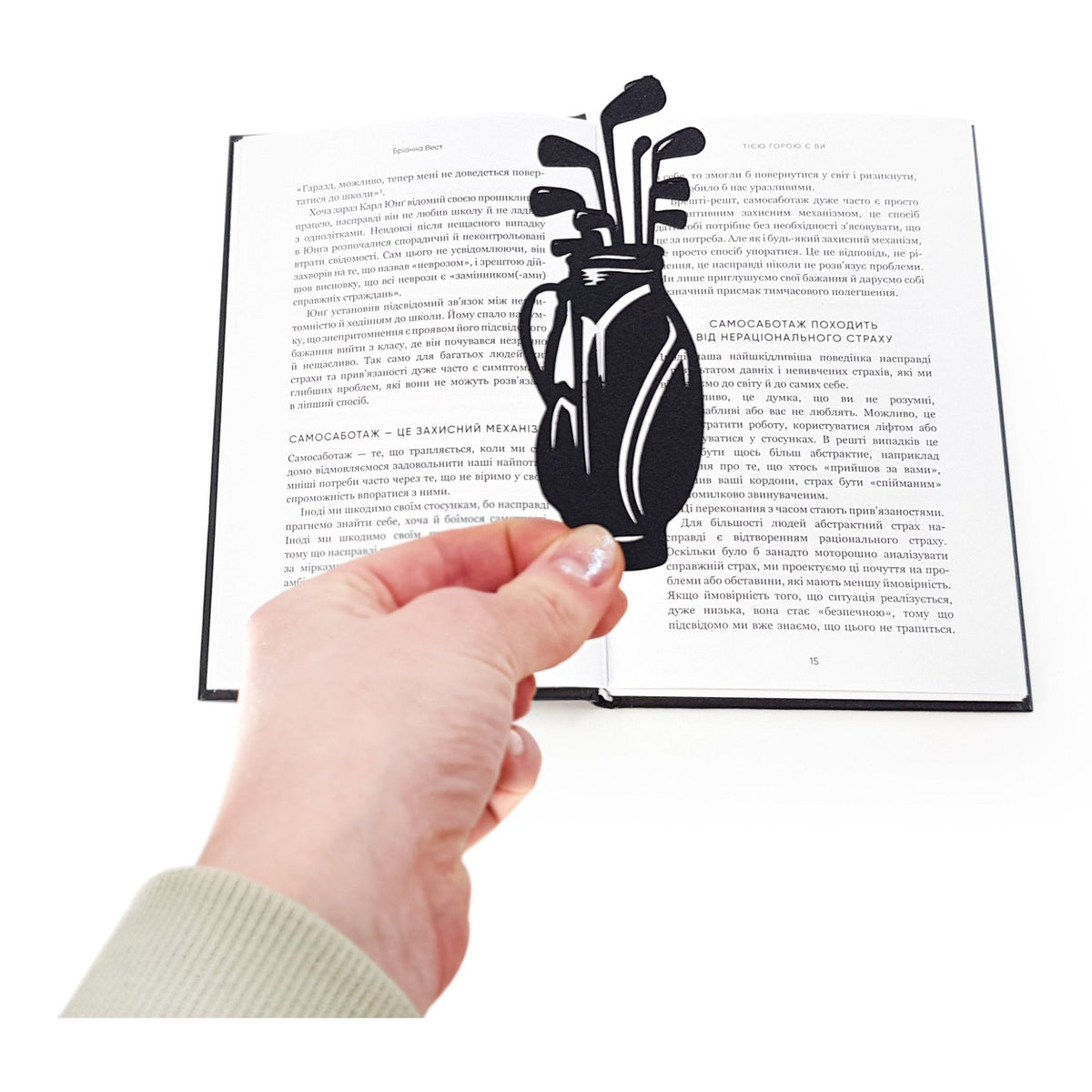 Golf Bag metal bookmark held in a hand above an open book