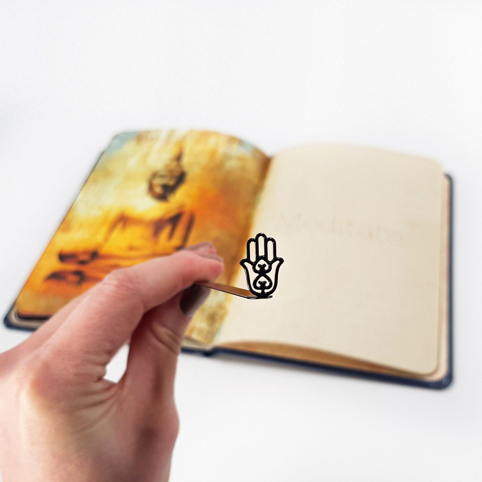 Hamsa metal bookmark held in a hand above an open book