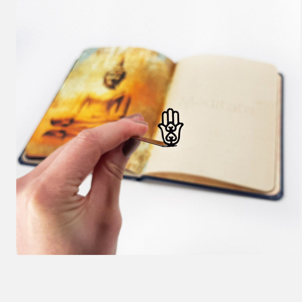 Hamsa metal bookmark held in a hand above an open book