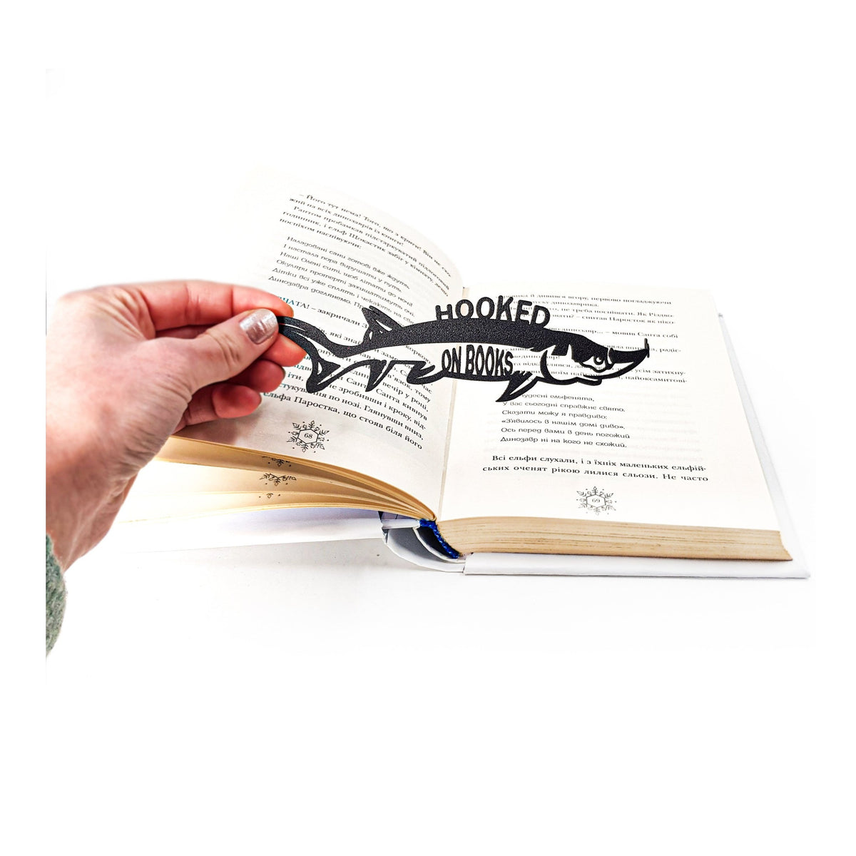 Hooked on Books metal bookmark held in a hand above an open book