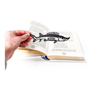 Hooked on Books metal bookmark held in a hand above an open book