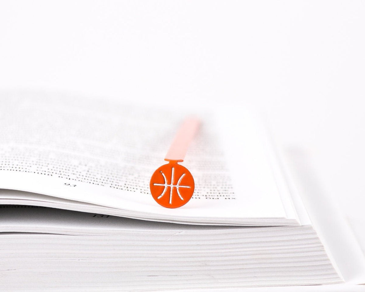 Hoop Dreams Mark metal bookmark in red resting on the pages of an open book