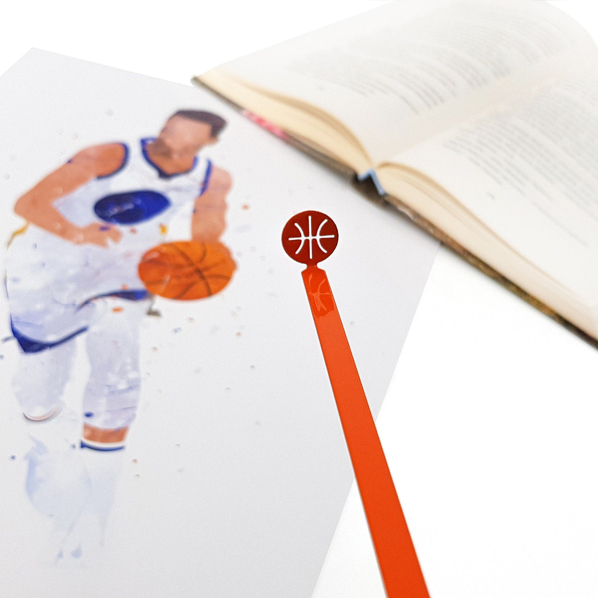 Hoop Dreams Mark metal bookmark in red marking a page in an illustrated book, view 4