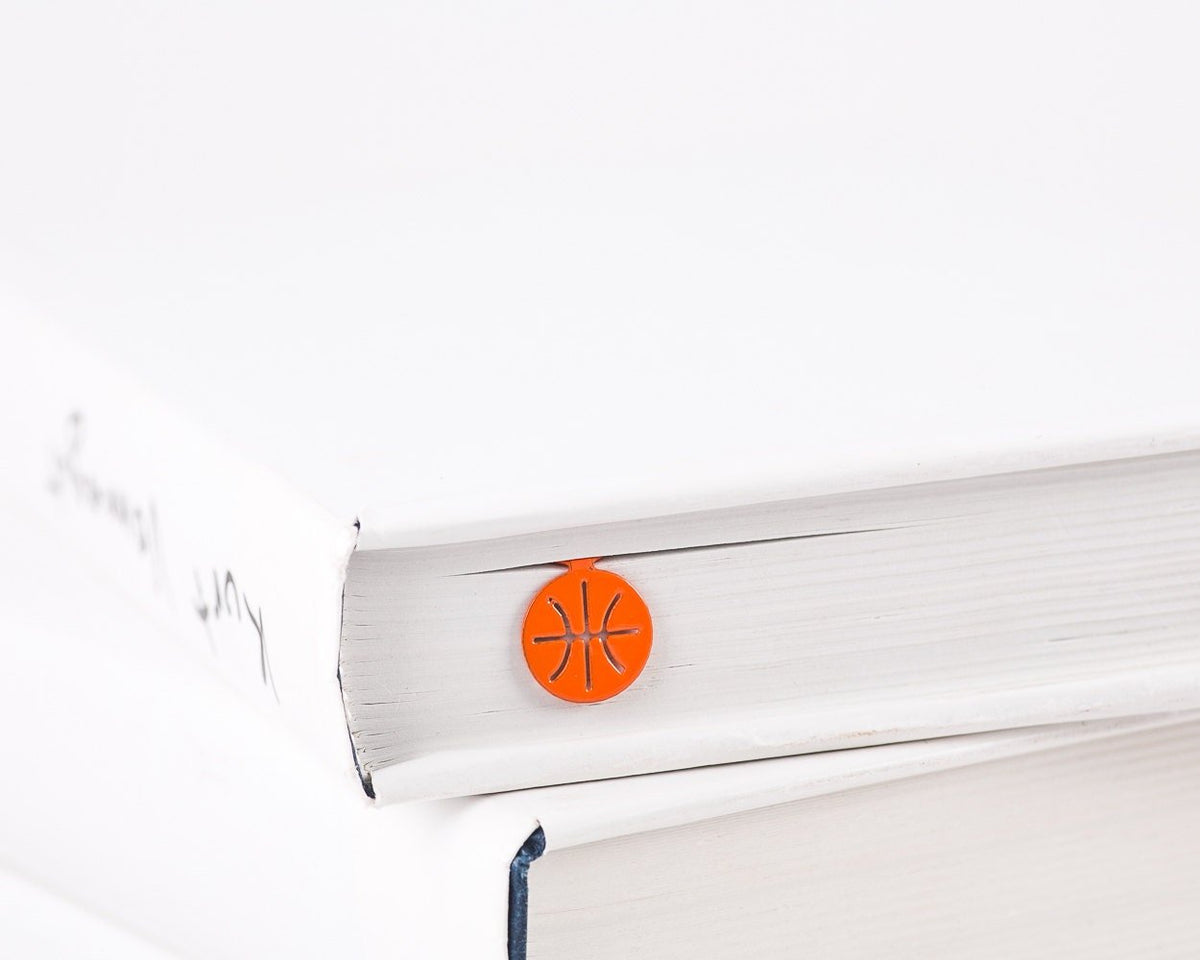 Hoop Dreams Mark metal bookmark in red in a closed book, only its top showing above the pages
