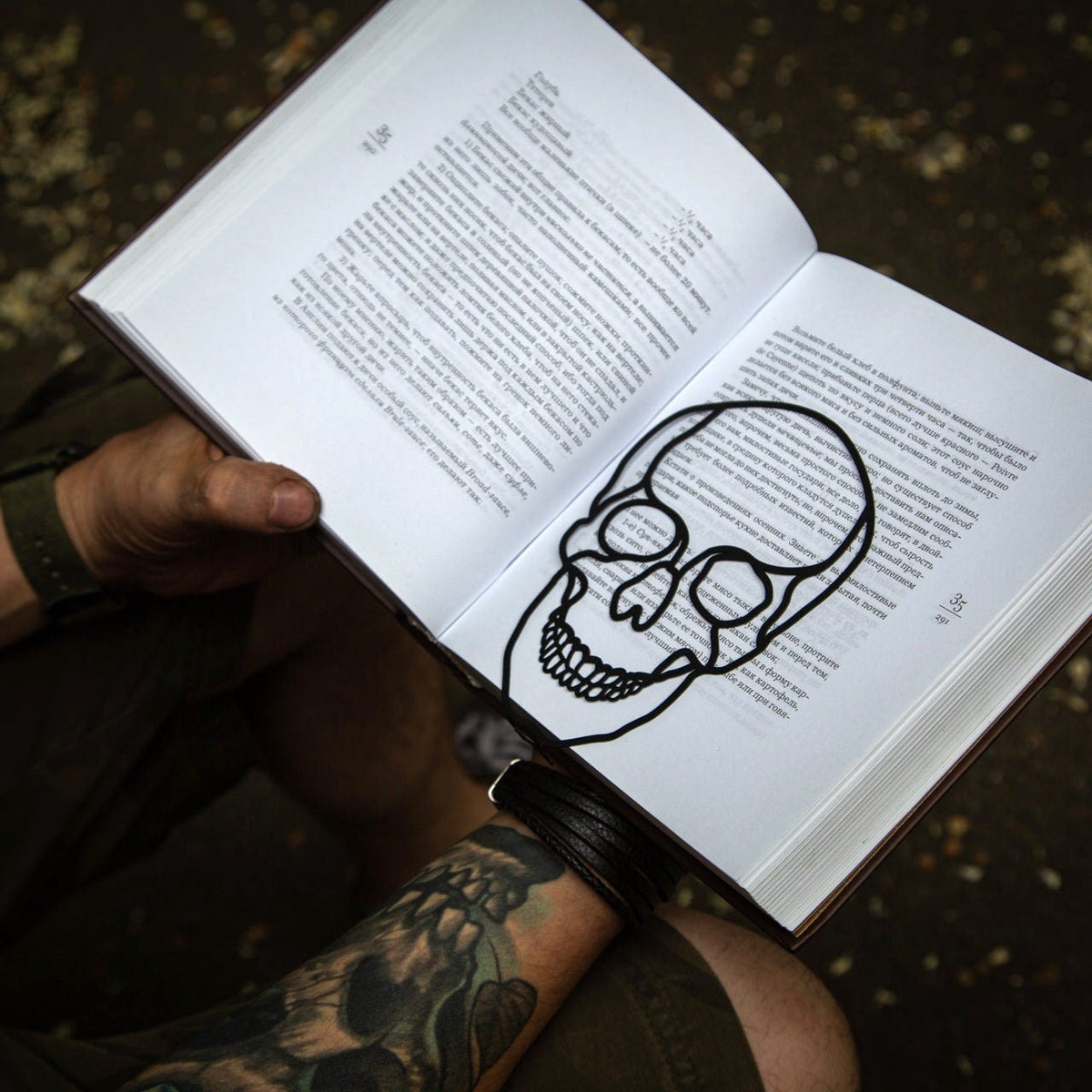 Horror Skull metal bookmark held in a hand above an open book