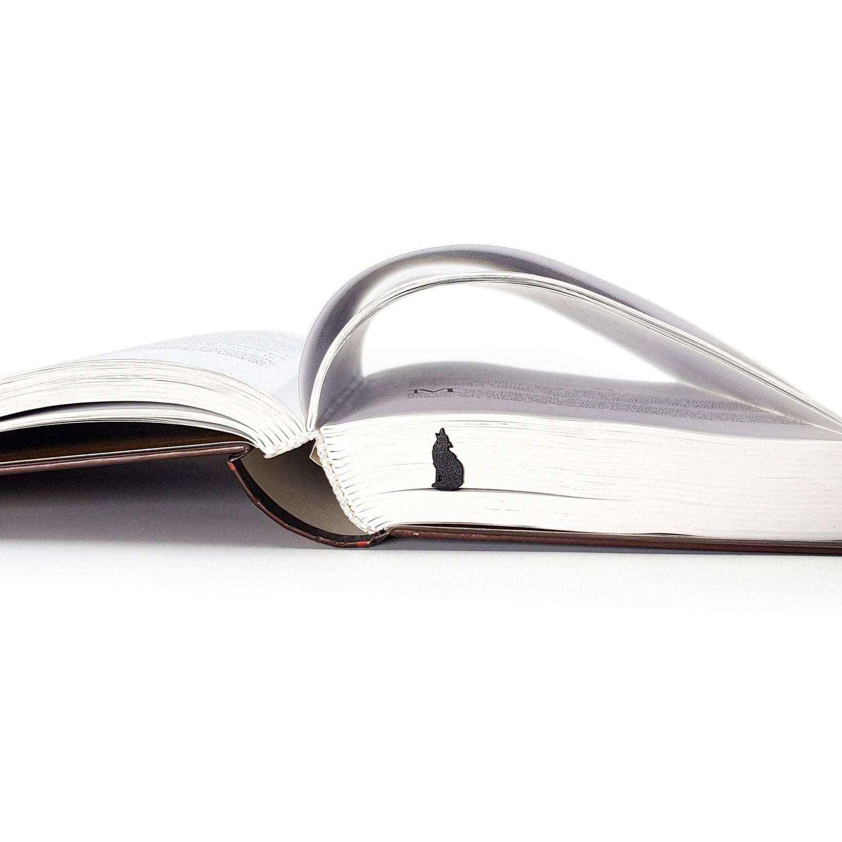 Howling Wolf metal bookmark clipped in a closed book, viewed from the side